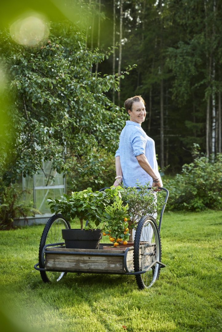 Raila står i sin trädgård med en vagn med små citrusträd. 